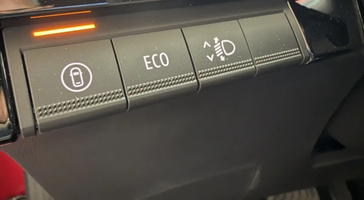 Gros plan sur les boutons de commande intérieurs de la Renault Clio 2025 rouge, avec mode ECO et réglage des phares.