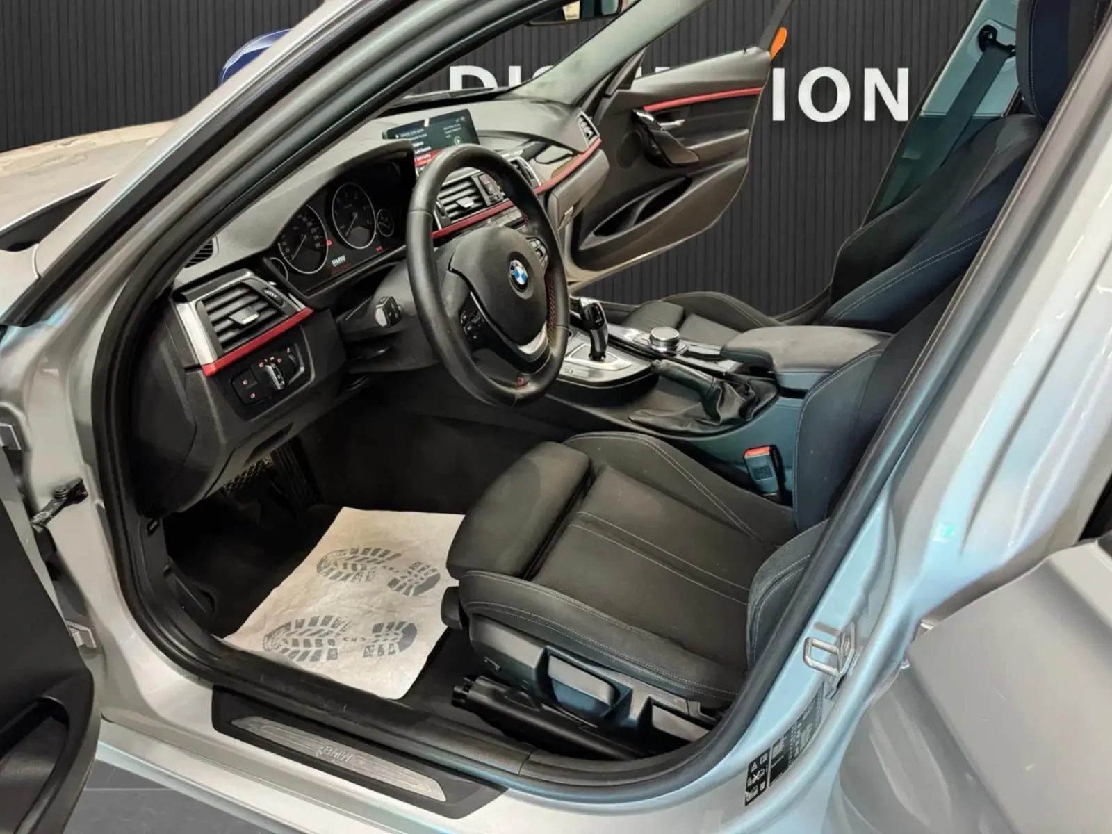 Vue intérieure côté conducteur d'une BMW Série 3 Touring gris aluminium, avec sièges noirs et tableau de bord sportif.