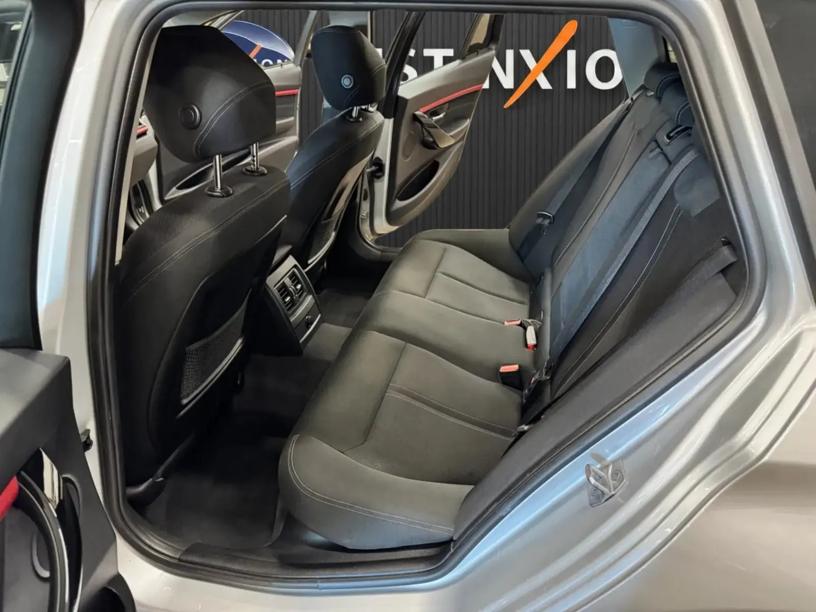 Vue intérieure côté gauche montrant la banquette arrière noire et la portière ouverte d'une BMW Série 3 Touring gris aluminium.
