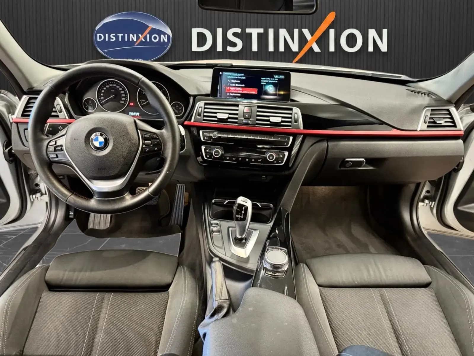 Vue intérieure avant de la BMW Série 3 Touring F31 320d XDrive 2018, tableau de bord noir avec bande rouge et écran central.