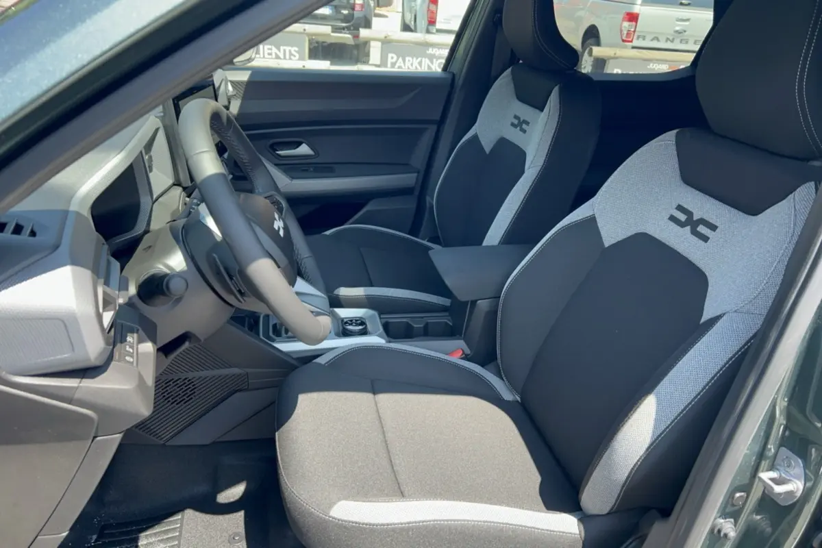 Vue intérieure côté conducteur du Dacia Duster Hybrid-G 150 4x4 en vert cèdre, sièges bi-ton avec logo distinctif sur appuie-tête.