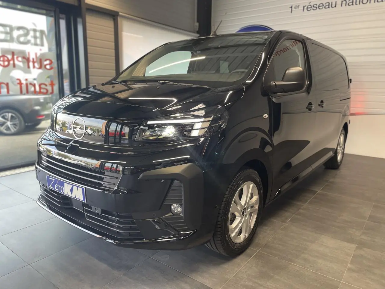 Opel Vivaro noir carbone en showroom, vue 3/4 avant droit avec phares allumés et jantes argentées.