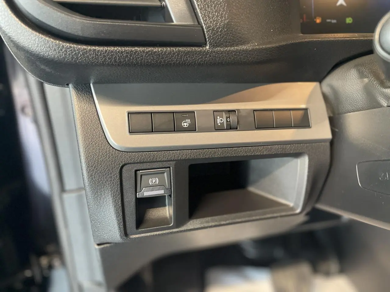 Gros plan sur les commandes de réglage des phares et frein à main électrique dans l'habitacle noir du Opel Vivaro 2025.