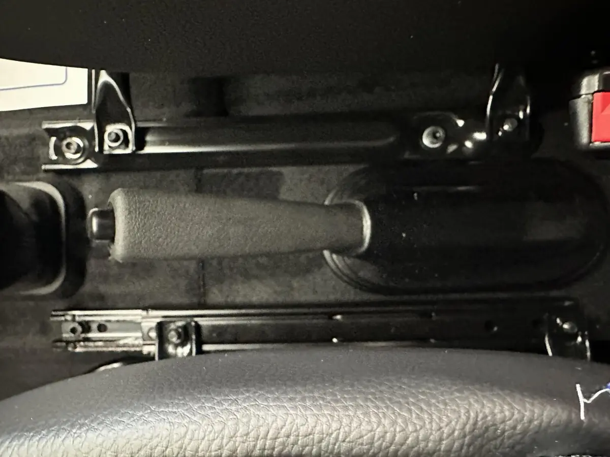 Gros plan sur le frein à main noir et la partie inférieure du siège en cuir dans l'habitacle de l'AIXAM Ambition bleu.