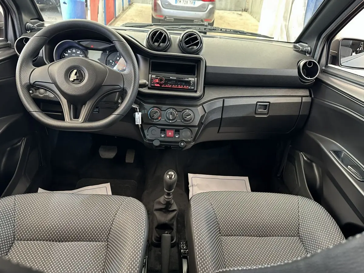 Vue intérieure avant de l'AIXAM AMBITION 0.5 CITY PACK 2026, tableau de bord noir avec volant et sièges gris à motifs.