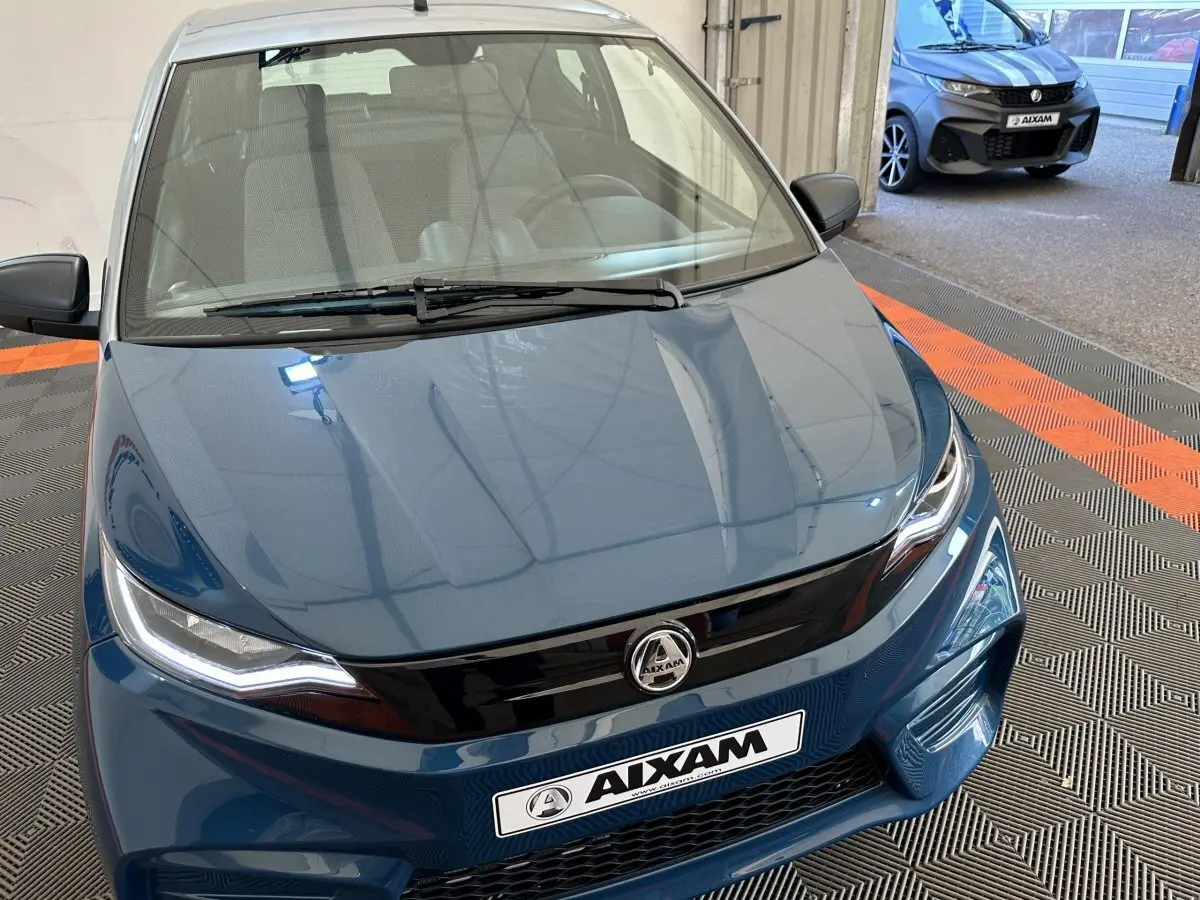 Vue avant plongeante sur l'AIXAM AMBITION 0.5 CITY PACK bleu avec calandre noire et rétroviseur caméra côté gauche.