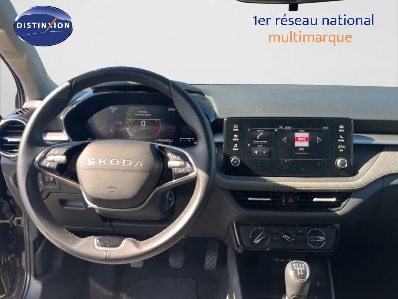 Vue intérieure centrée sur le volant SKODA et le tableau de bord avec écran tactile, ambiance gris noir moderne.