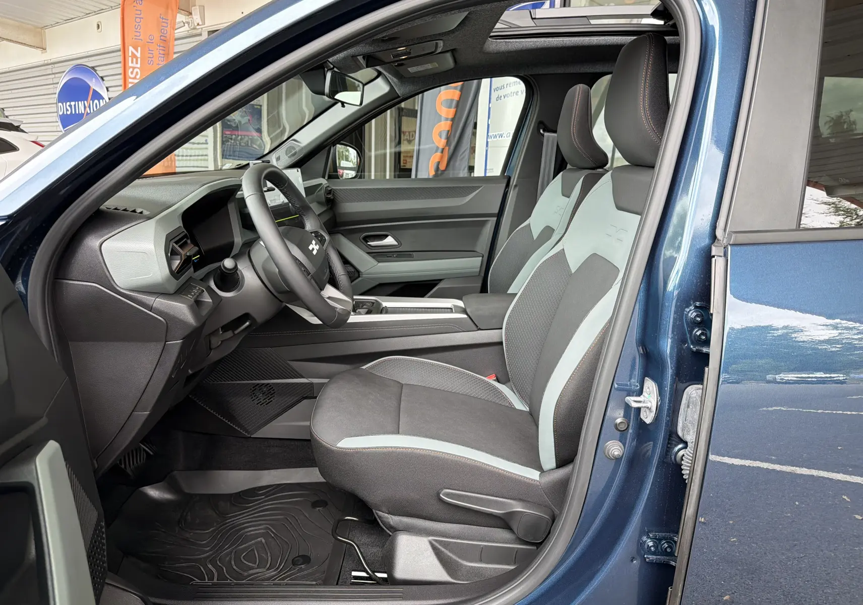 Vue intérieure côté conducteur du Dacia Bigster bleu indigo, mettant en valeur les sièges bicolores et le tableau de bord moderne.