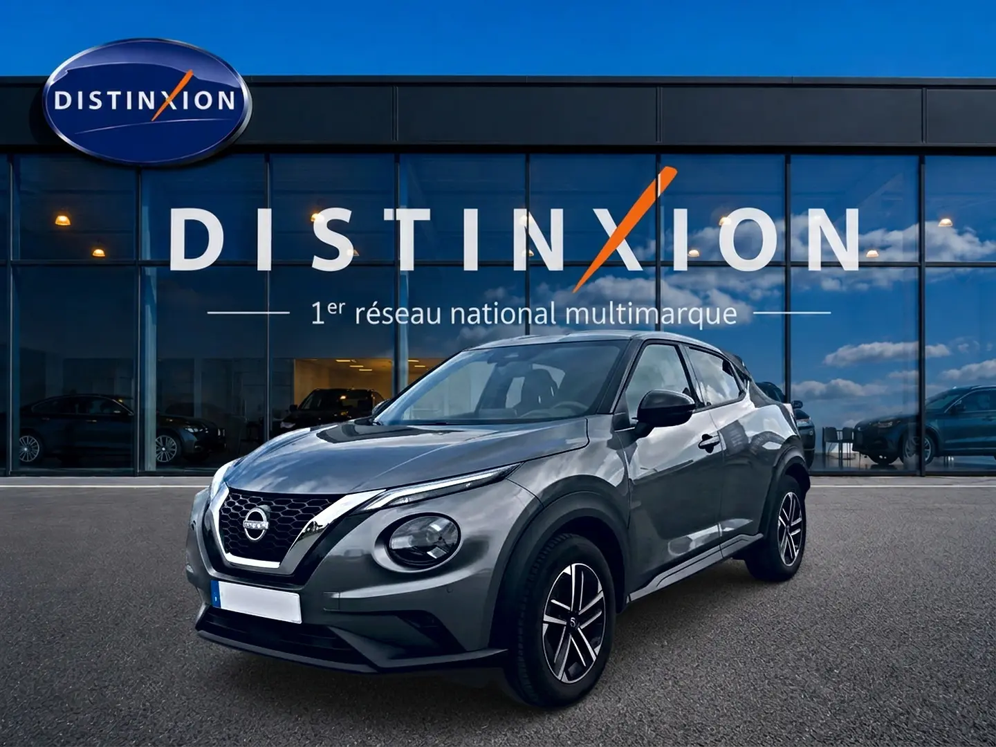 Nissan Juke gris 2025 en 3/4 avant droit, avec jantes alu et calandre noire brillante devant showroom Distinxion.
