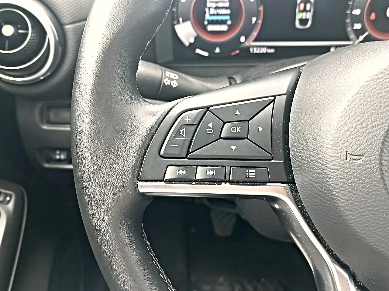 Gros plan sur le volant cuir noir multifonction du Nissan Juke gris, avec commandes audio et écran numérique en arrière-plan.