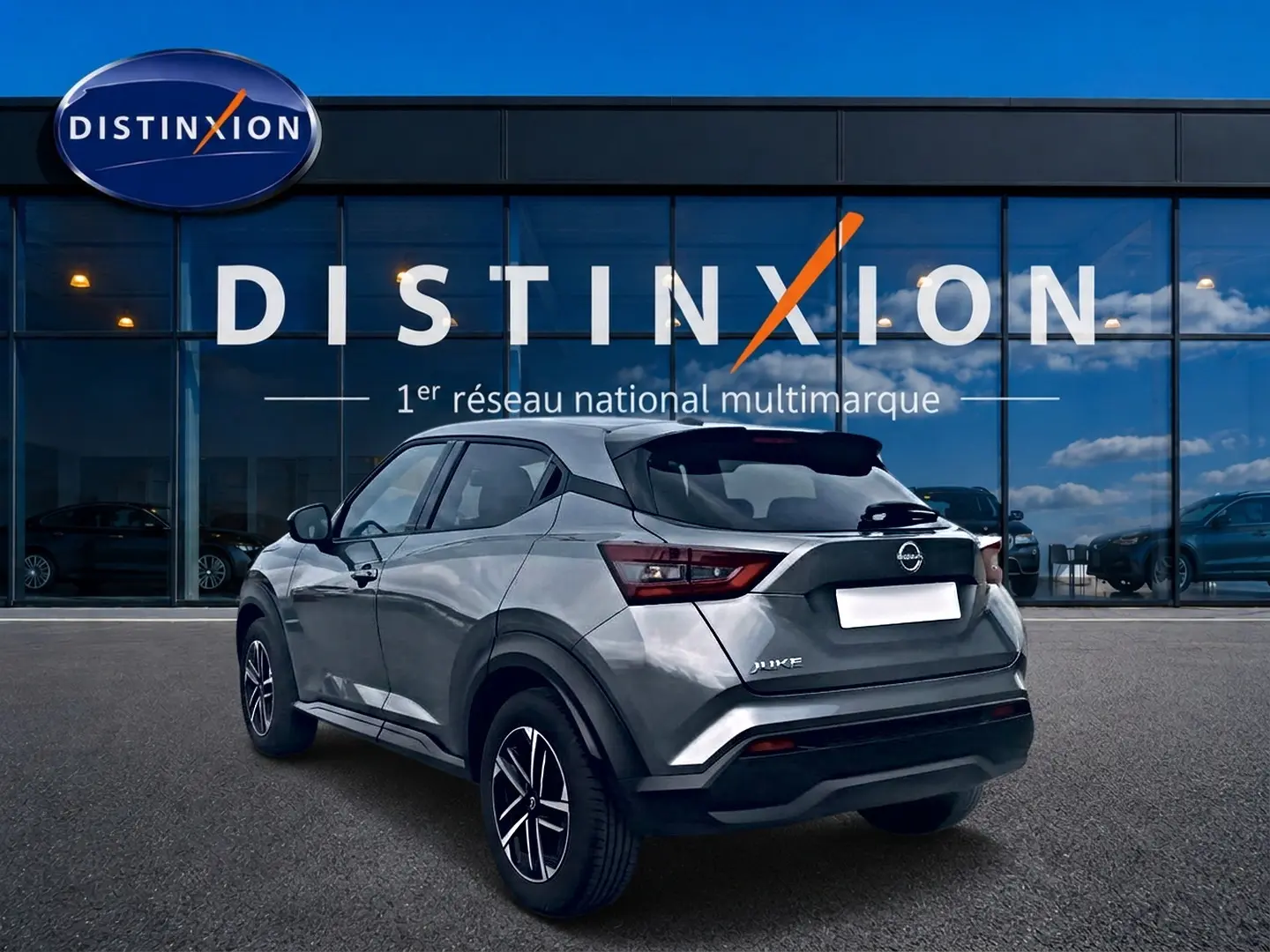 Nissan Juke gris vue 3/4 arrière droit, avec jantes alu et feux arrière LED, devant un showroom Distinxion.