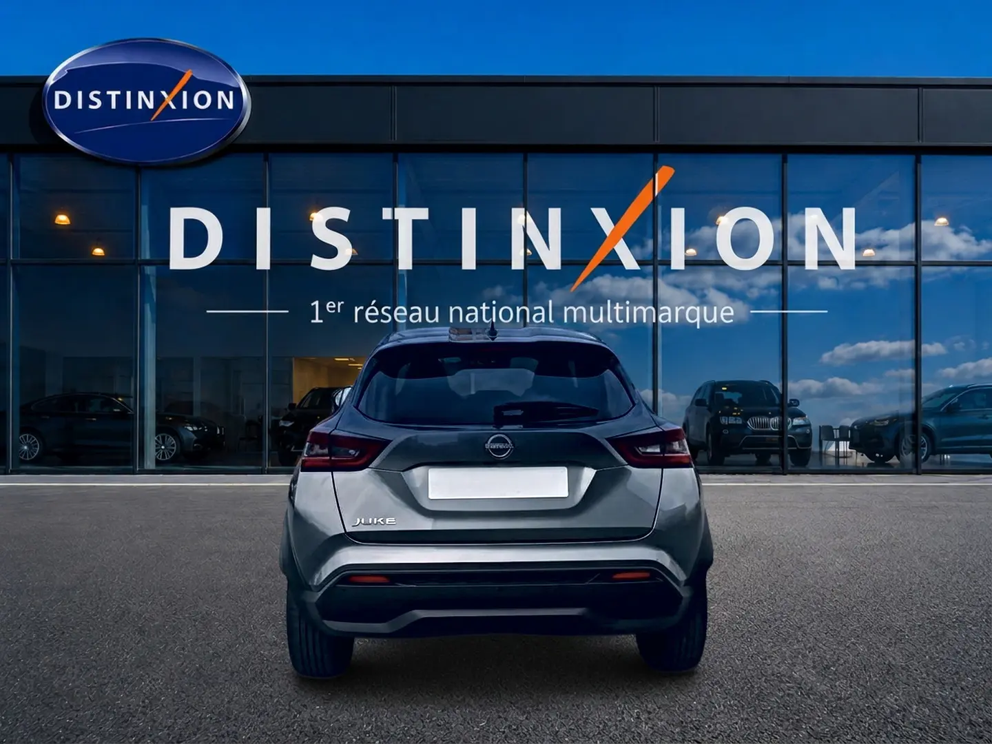 Vue arrière d'un Nissan Juke gris 2025 garé devant une vitrine avec logo Distinxion.