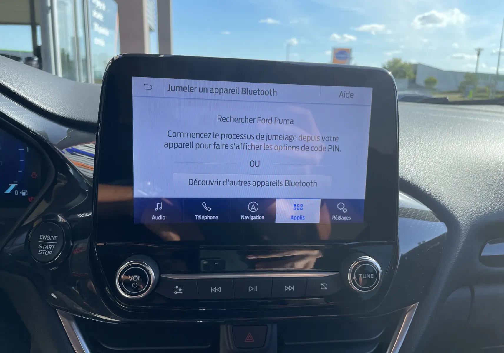 Écran tactile central du Ford Puma 2021 affichant le jumelage Bluetooth, avec boutons de volume et réglage sous un ciel ensoleillé.