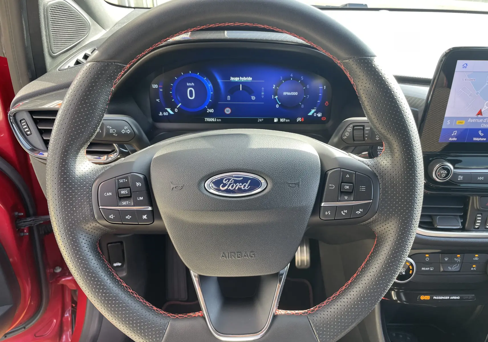 Vue rapprochée du volant perforé avec surpiqûres rouges et tableau de bord digital du Ford Puma rouge 2021.