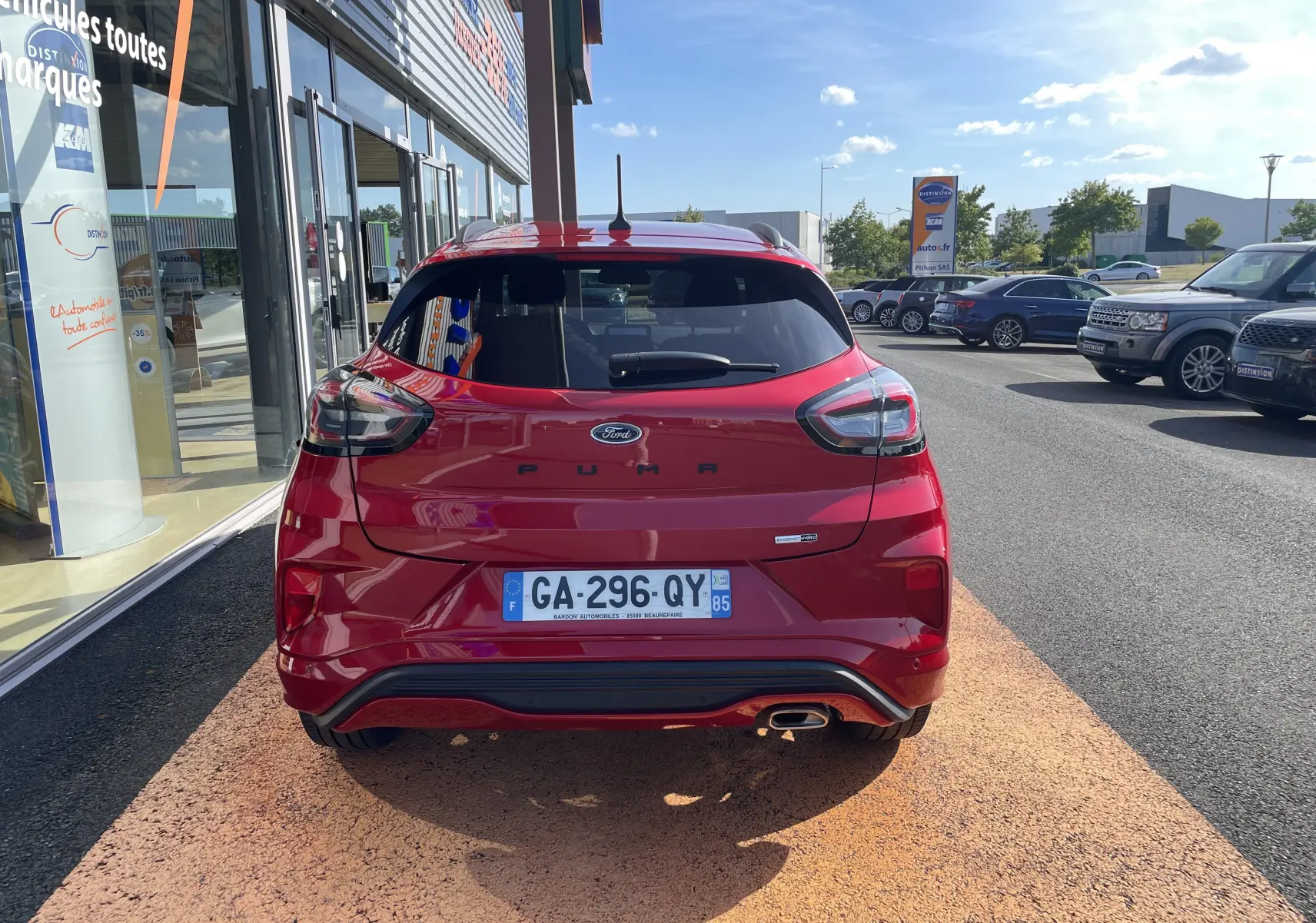 Vue arrière d'une Ford Puma rouge 2021 avec feux LED et sortie d'échappement chromée, stationnée devant un showroom.