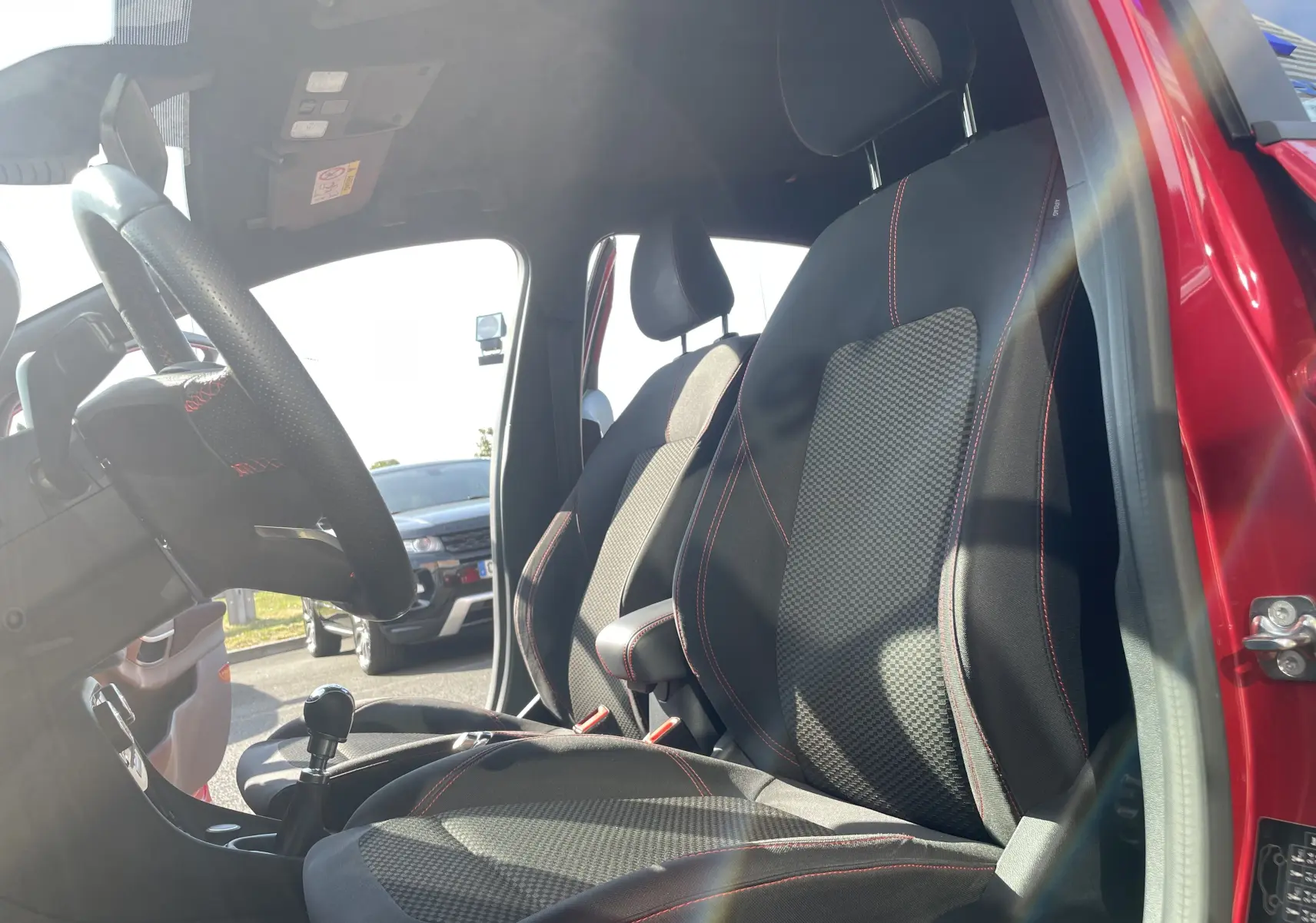 Intérieur du Ford Puma rouge 2021, vue côté gauche sur sièges en tissu noir avec surpiqûres rouges et levier de vitesses manuel.