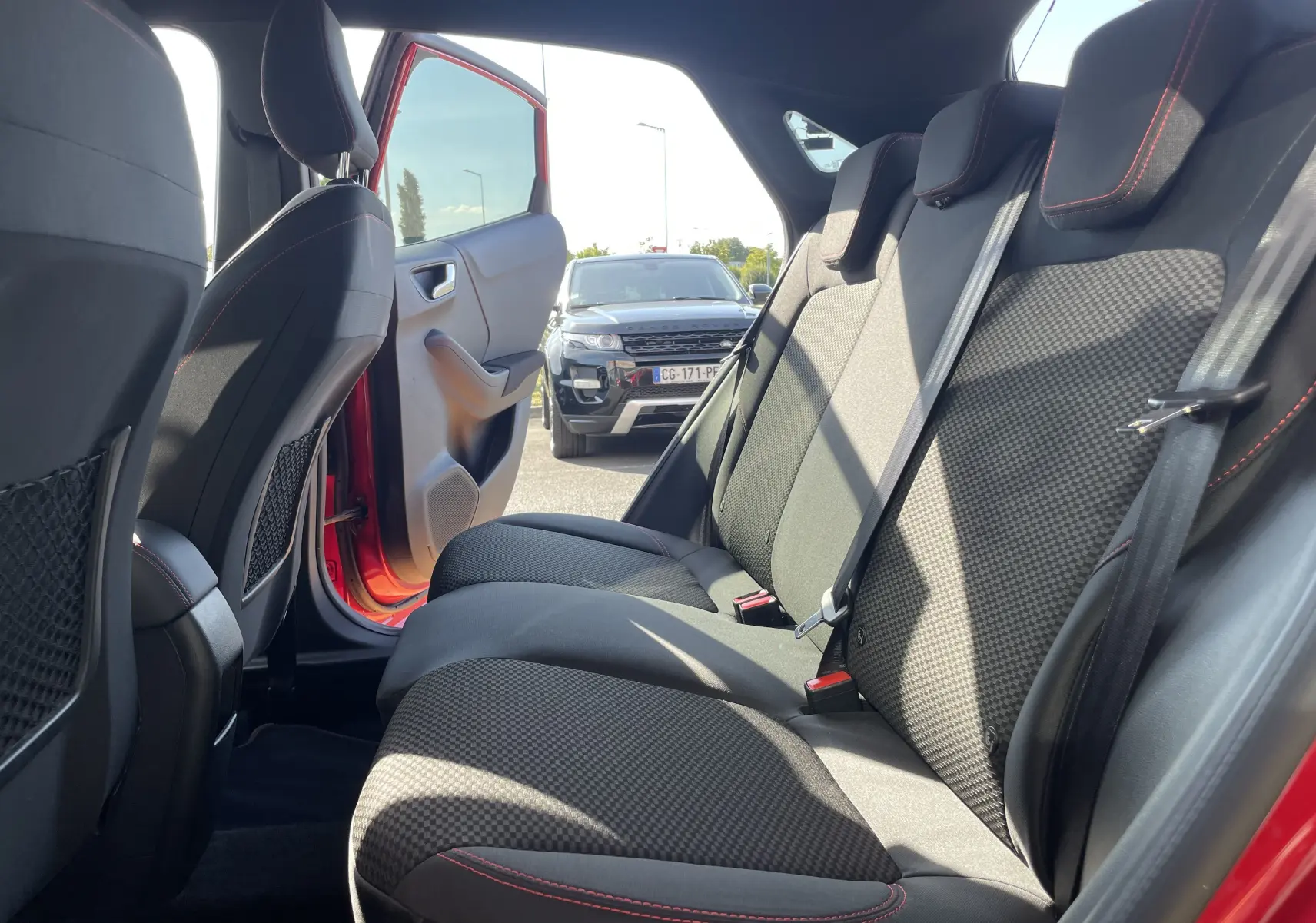 Vue intérieure arrière droite du Ford Puma rouge 2021, montrant les sièges arrière en tissu noir avec surpiqûres rouges.