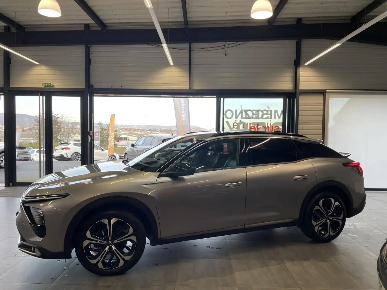 Vue de profil côté gauche d'une Citroën C5 X 2024 gris foncé, soulignant ses jantes noires et son design élancé.