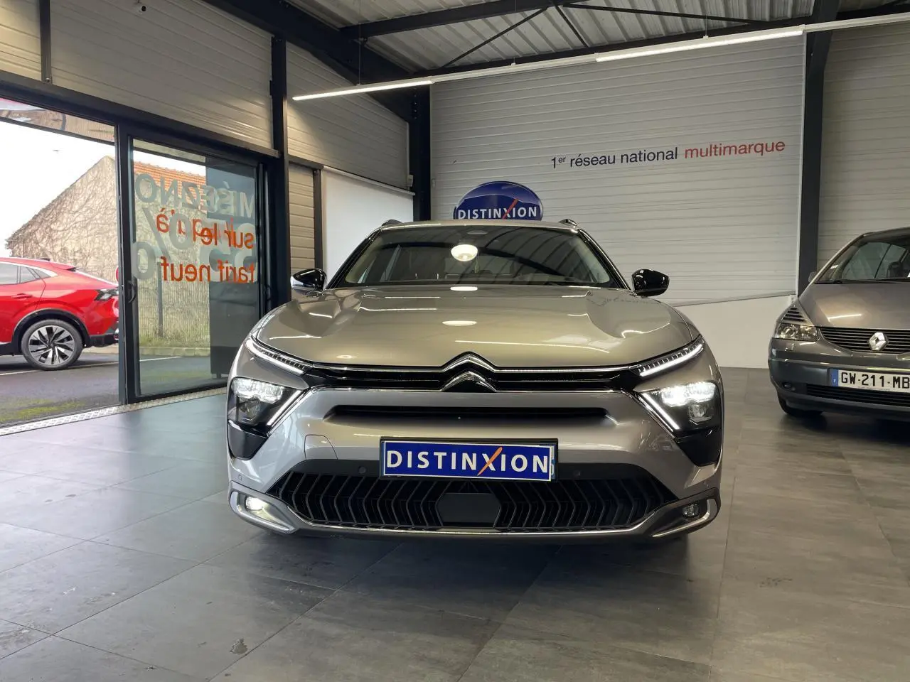 Vue avant d'un Citroën C5 X 2024 gris foncé avec calandre distinctive et phares allumés en showroom.