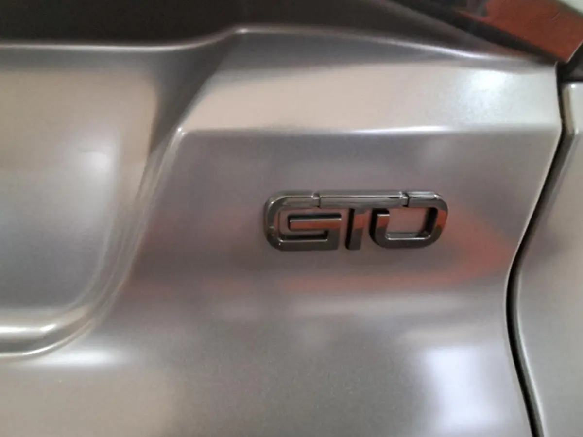 Gros plan sur l’inscription GTO en relief sur la carrosserie gris clair de l’Aixam Ambition 2024.