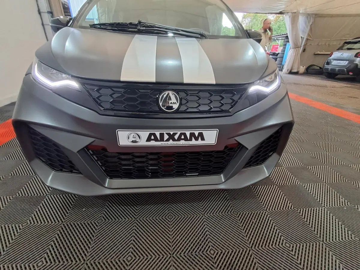 Vue frontale rapprochée de l'AIXAM AMBITION gris clair avec bandes blanches et éclairage LED distinctif.