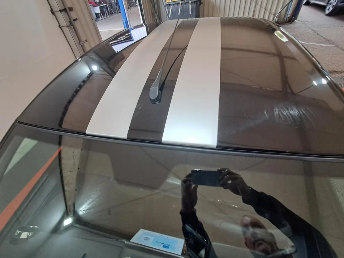 Vue plongeante sur le toit gris clair de l'AIXAM AMBITION 2024 avec bandes blanches sportives et antenne centrale.