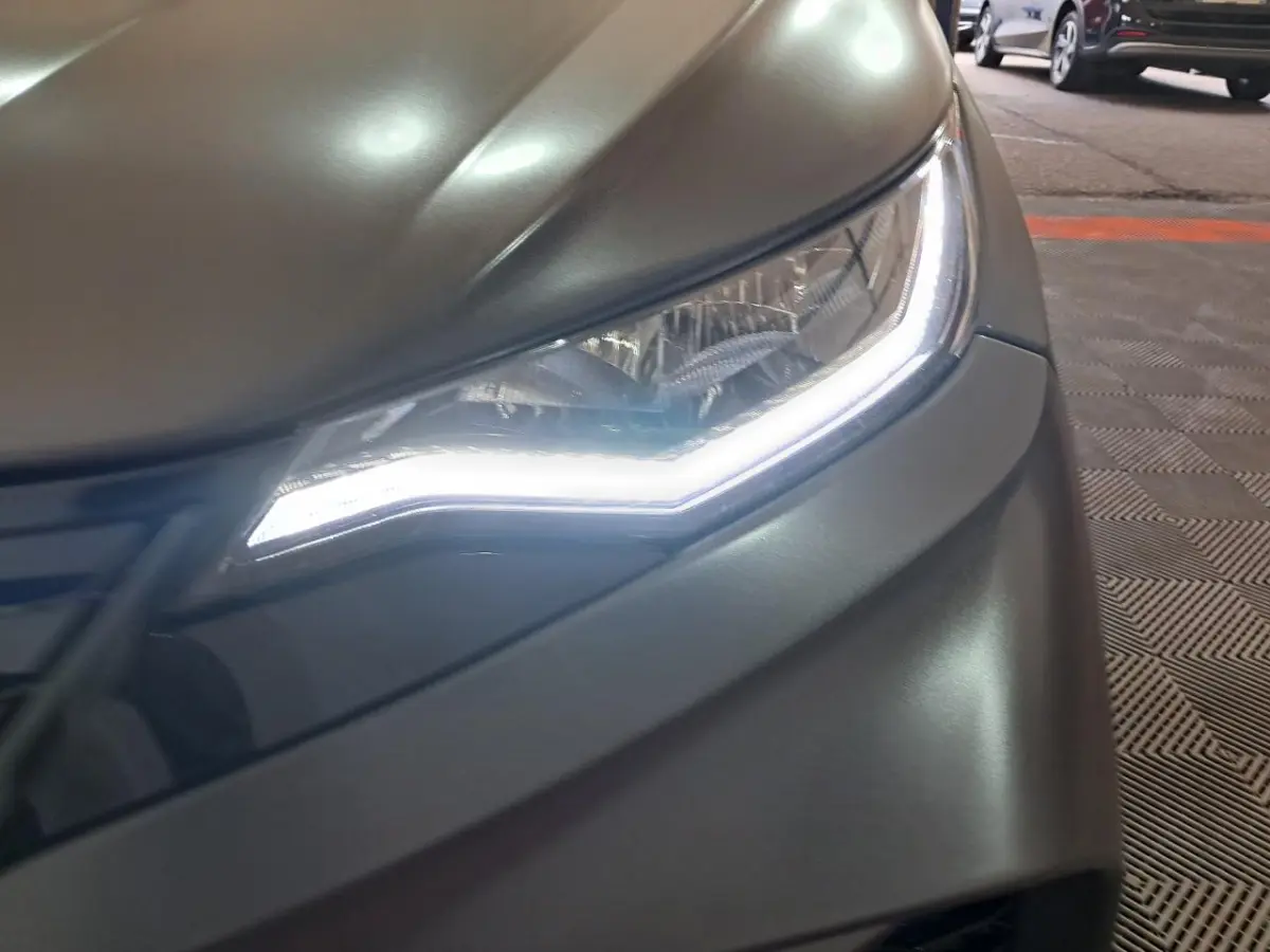 Gros plan sur le phare avant droit d'une Aixam Ambition 2024 gris clair avec éclairage LED distinctif.