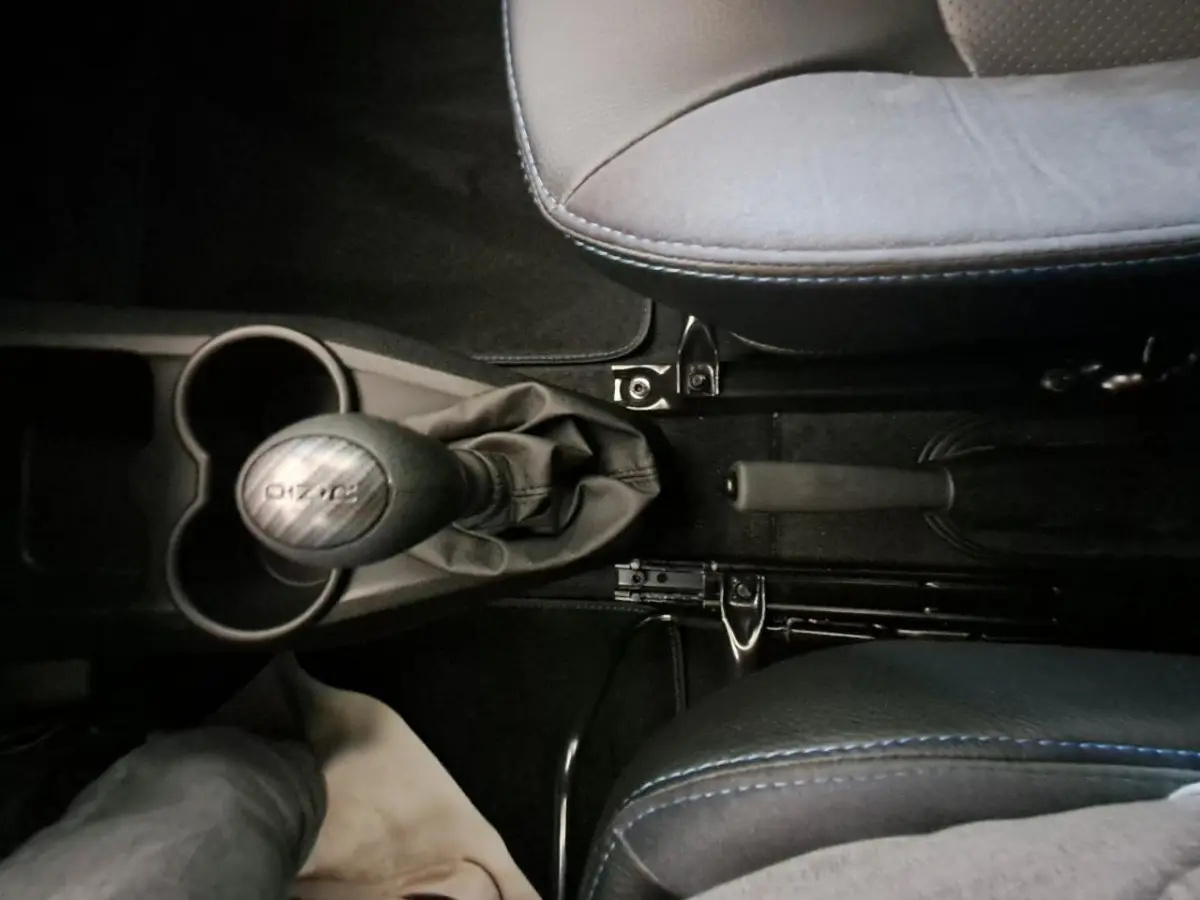 Vue plongeante sur la console centrale de l'AIXAM AMBITION 2024, avec levier de vitesse et frein à main entre sièges gris clair.