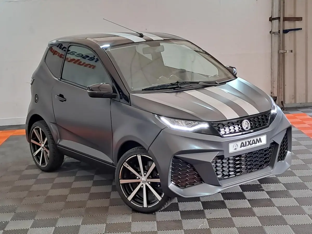 Aixam Ambition 2024 gris clair en 3/4 avant droit avec bandes blanches et jantes alliage noires diamantées.