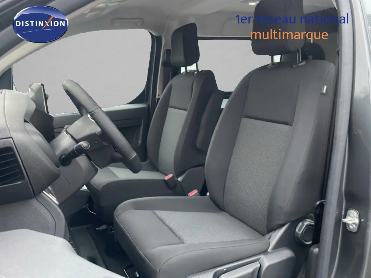 Vue intérieure côté conducteur du Citroën Jumpy Long L3 gris titane, montrant les sièges avant en tissu noir et gris.