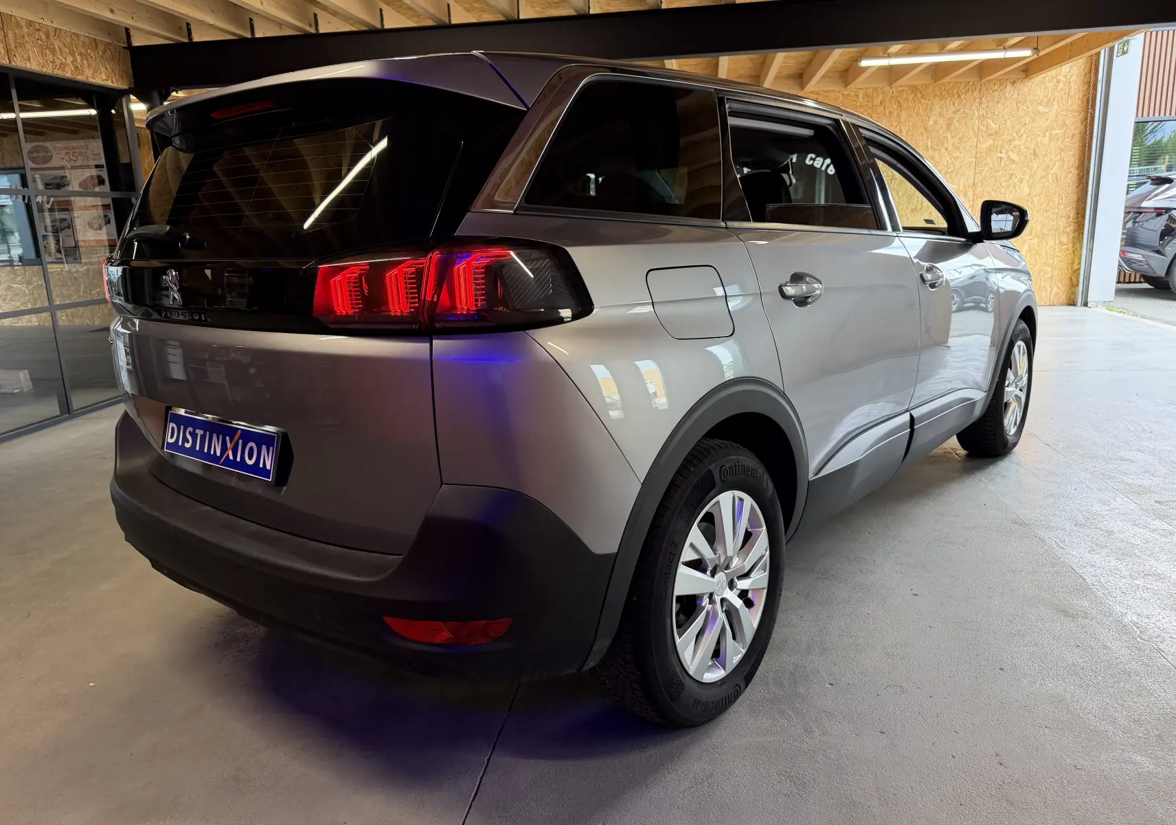 Vue 3/4 arrière droit d’un Peugeot 5008 gris 2021 avec feux arrière LED et jantes alliage en intérieur d’exposition.