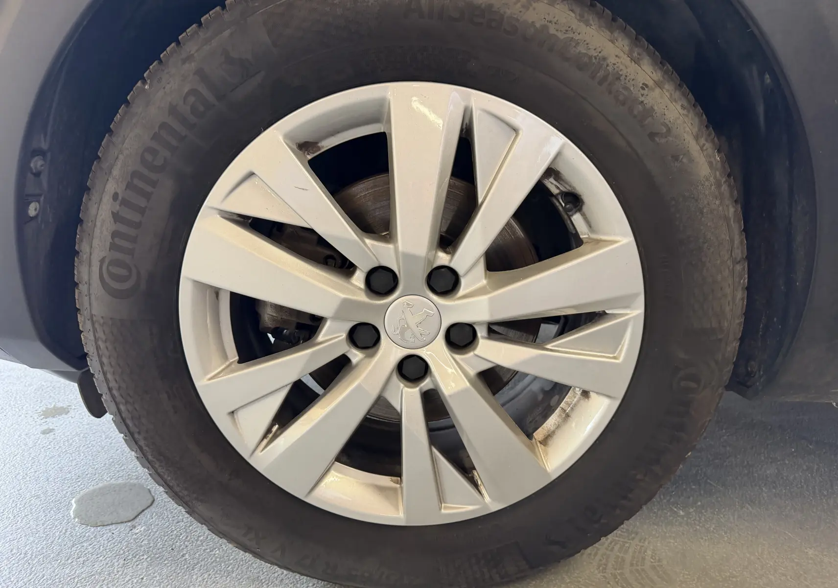Gros plan sur la roue avant droite d’un Peugeot 5008 gris, avec jante alliage et logo Peugeot au centre.