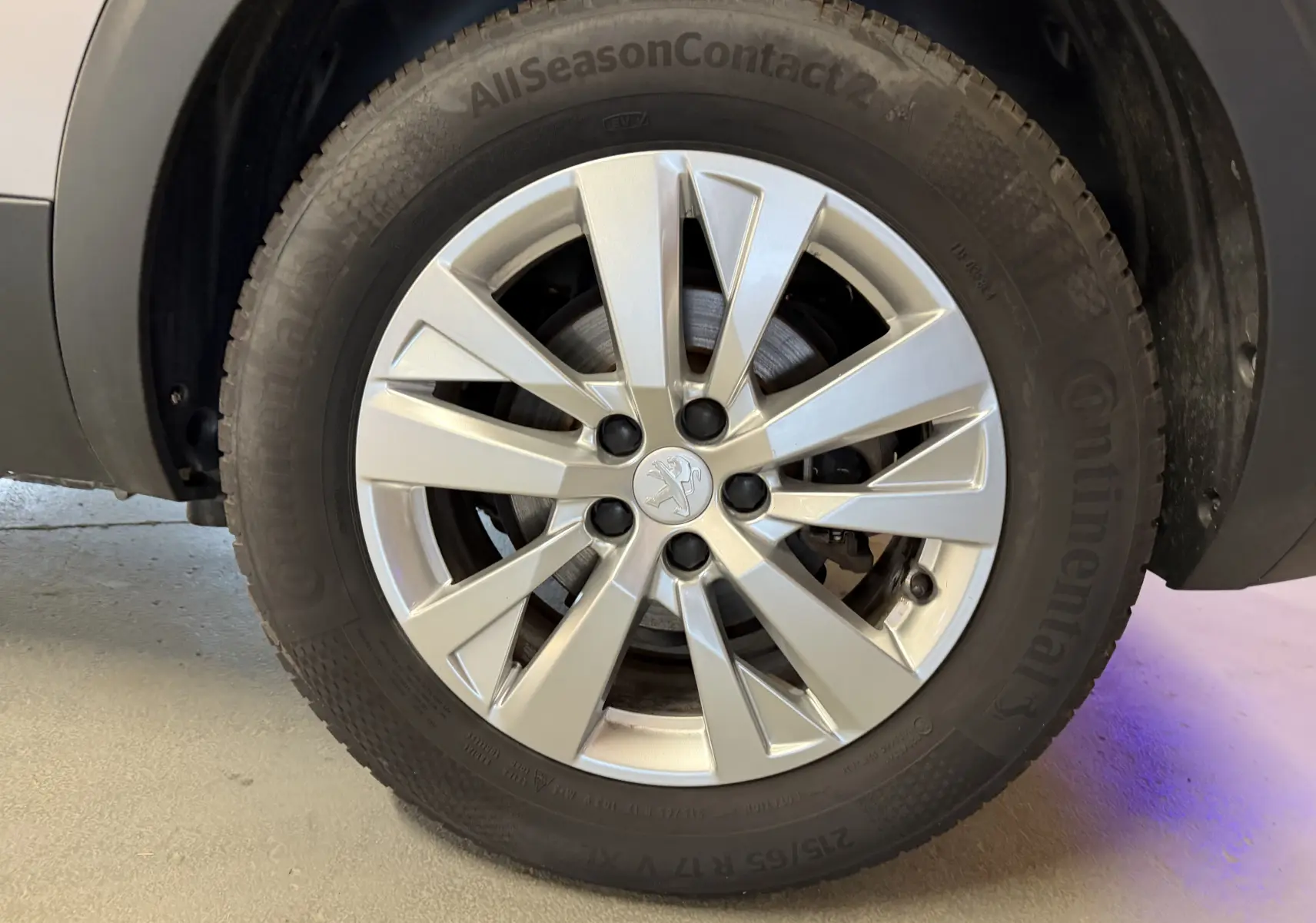 Gros plan sur la roue avant droite d’un Peugeot 5008 gris, jante alliage argentée avec logo Peugeot central.