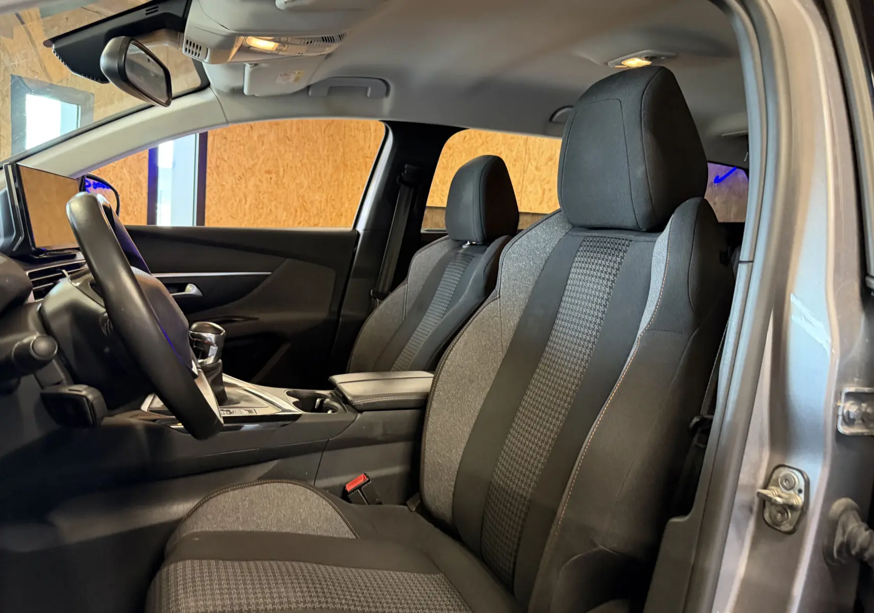 Vue intérieure côté conducteur du Peugeot 5008 gris 2021, mettant en valeur les sièges en tissu noir et la console centrale.
