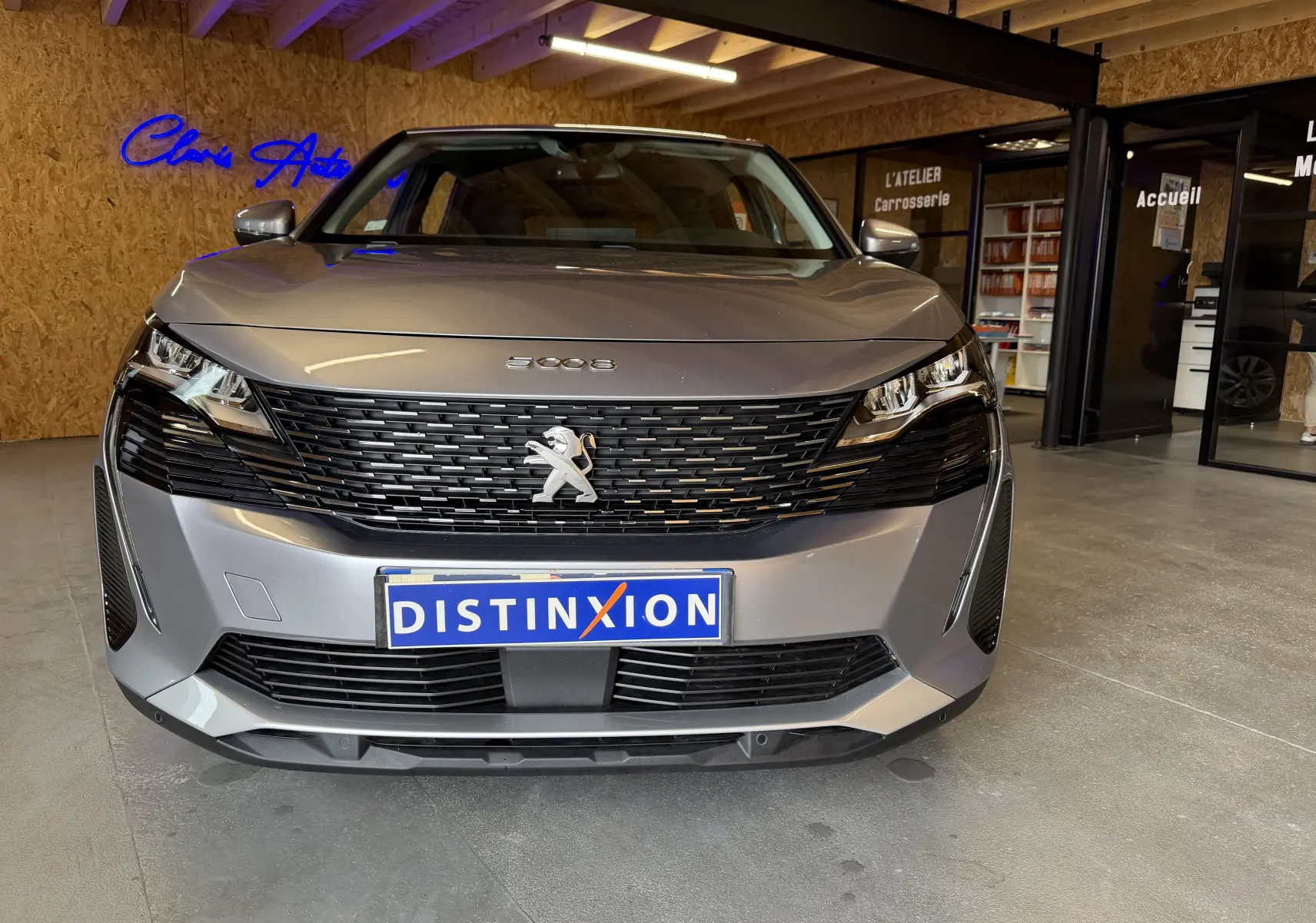 Vue frontale d’un Peugeot 5008 gris 2021 avec calandre noire et logo lion au centre, en intérieur showroom.