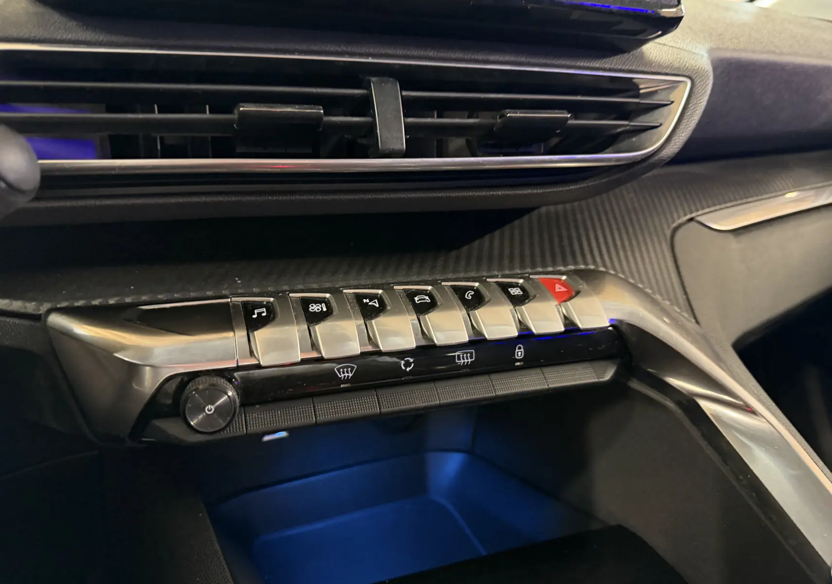 Vue rapprochée de la console centrale du Peugeot 5008 gris, mettant en valeur les commandes piano et l’éclairage d’ambiance bleu.