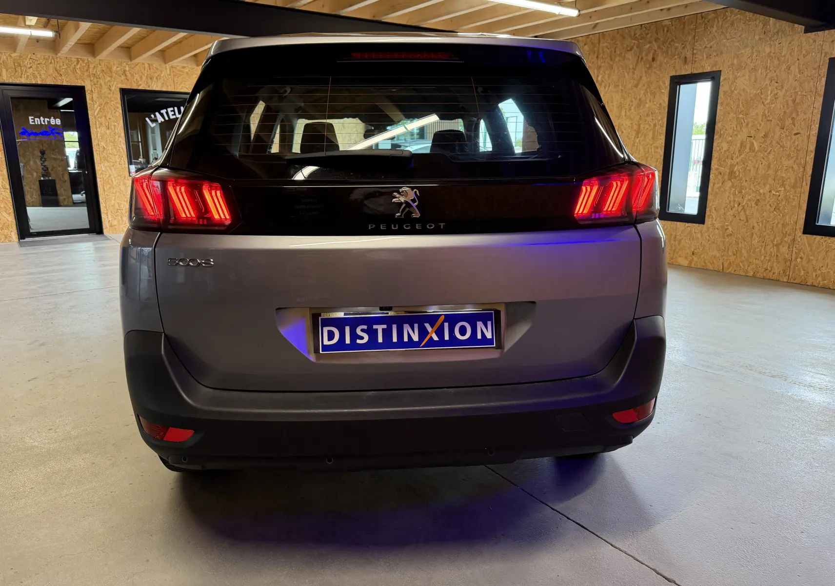 Vue arrière d’un Peugeot 5008 gris 2021 avec feux arrière allumés dans un garage lumineux.