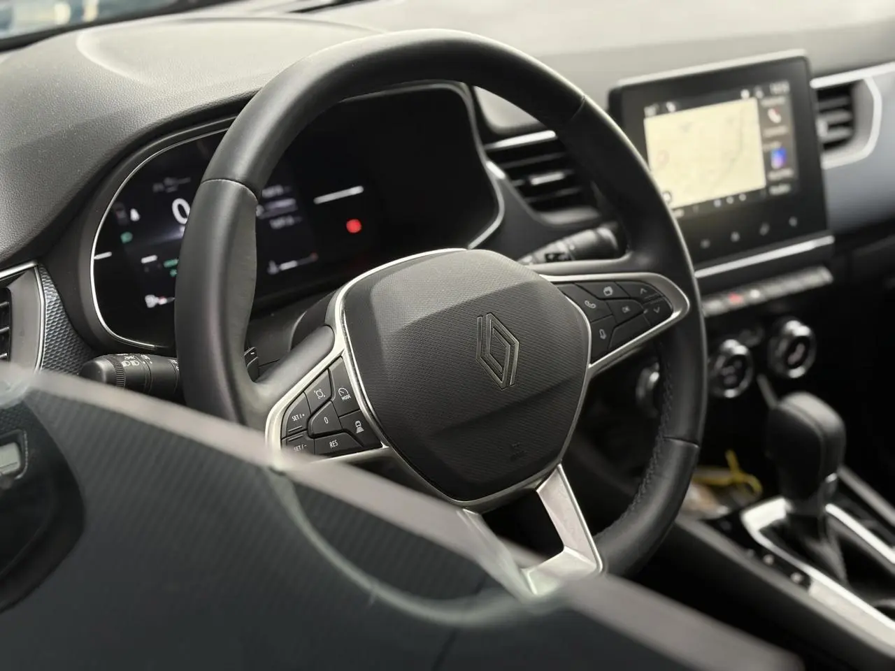 Vue rapprochée du volant noir et du tableau de bord numérique de la Renault Arkana 2025 avec écran tactile GPS.