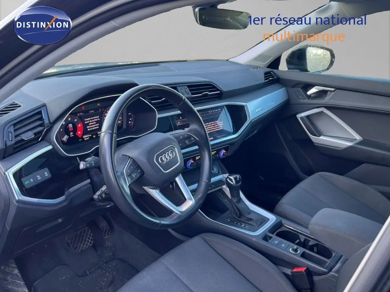 Intérieur de l'Audi Q3 Sportback 2022 vu côté conducteur, tableau de bord moderne avec écran tactile et volant cuir noir.