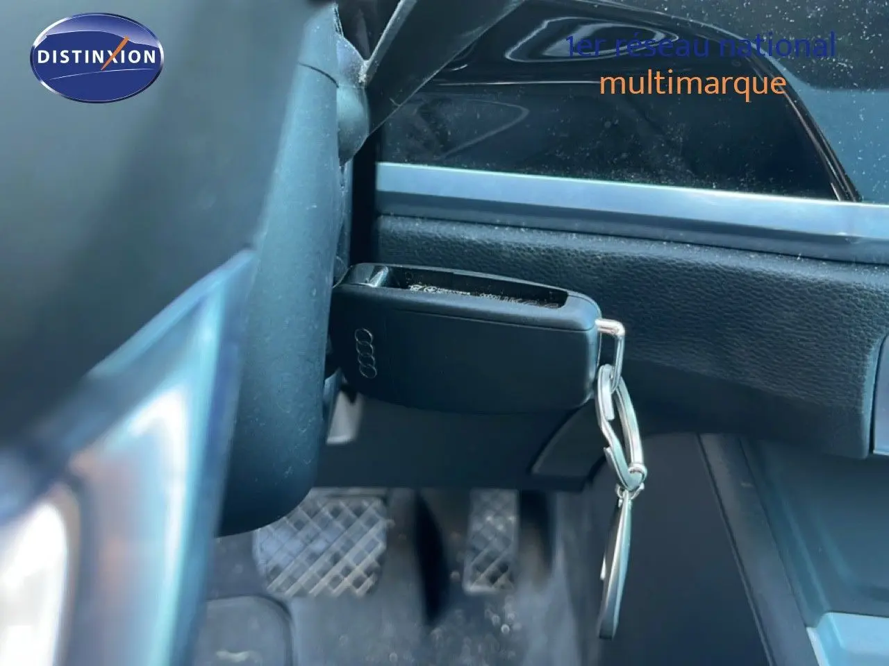 Gros plan sur la clé Audi accrochée sous le volant, avec vue partielle du tableau de bord noir intérieur du Q3 Sportback.
