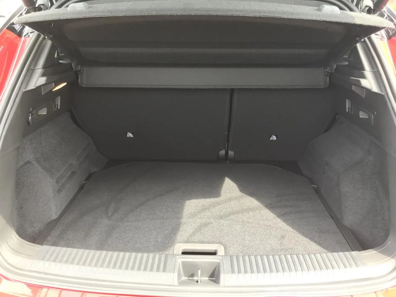 Coffre ouvert vu de l'arrière du Renault Austral rouge et noir, montrant l'espace de chargement vide et la moquette grise.