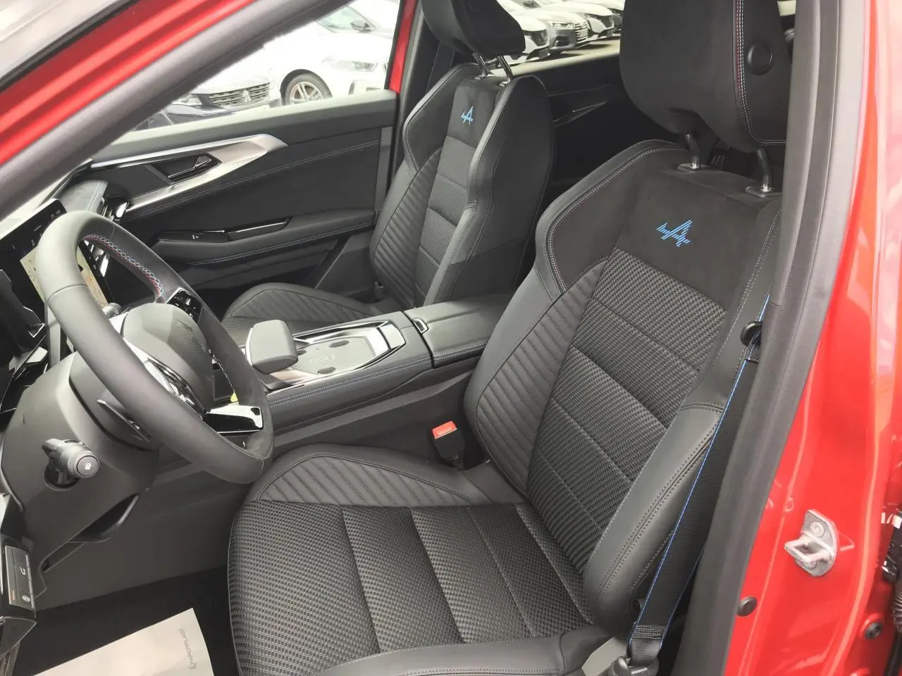 Vue intérieure côté conducteur du Renault Austral Esprit Alpine rouge et noir, mettant en valeur les sièges sport noirs avec surpiqûres bleues et logo Alpine brodé.