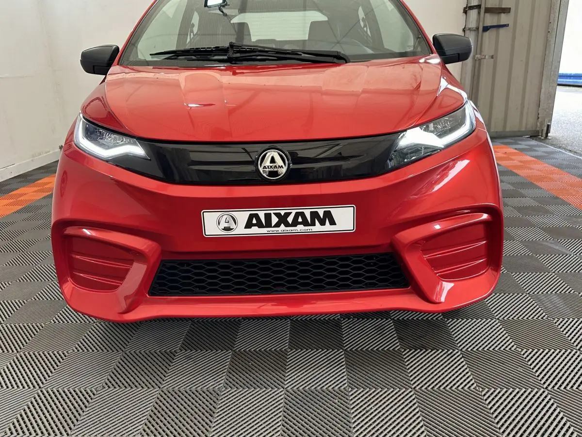 Vue frontale d'une Aixam Ambition E City Pack rouge 2026 avec calandre noire et phares LED allumés.