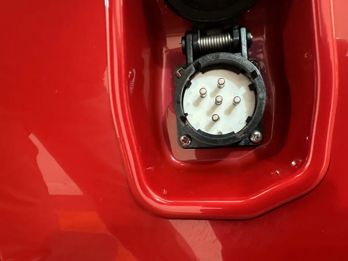 Gros plan sur la prise de recharge électrique intégrée dans la carrosserie rouge de l'AIXAM AMBITION E CITY PACK 2026.