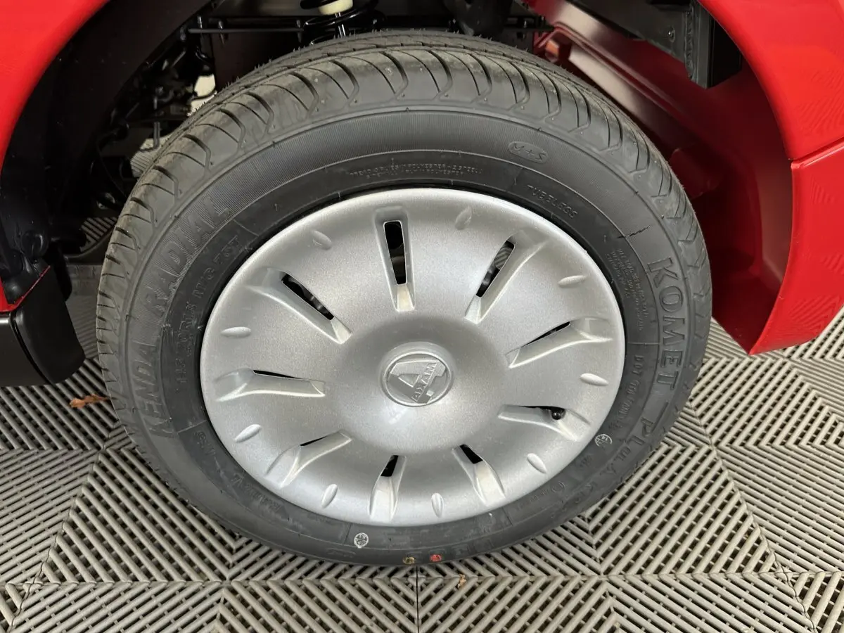 Gros plan sur la roue avant gauche d'une Aixam Ambition E City Pack rouge avec enjoliveur argenté et logo central.