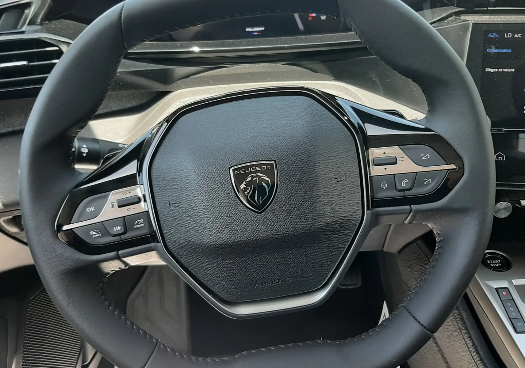 Vue rapprochée du volant noir de la Peugeot 308 III Ph.2 avec logo lion et commandes intégrées, intérieur gris selenium.