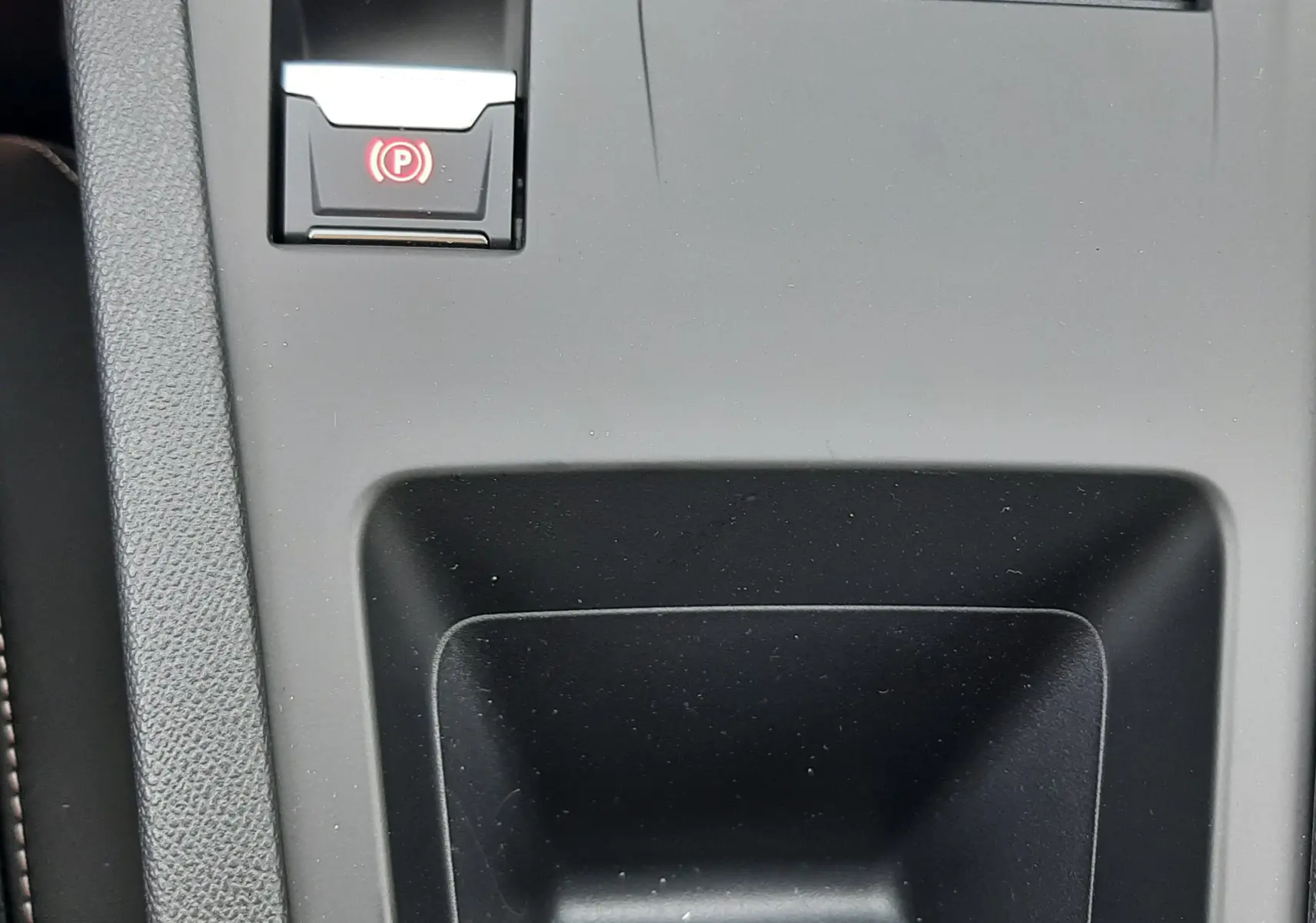 Gros plan sur la console centrale noire de la Peugeot 308 III Ph.2 avec bouton de frein à main électrique illuminé en rouge.