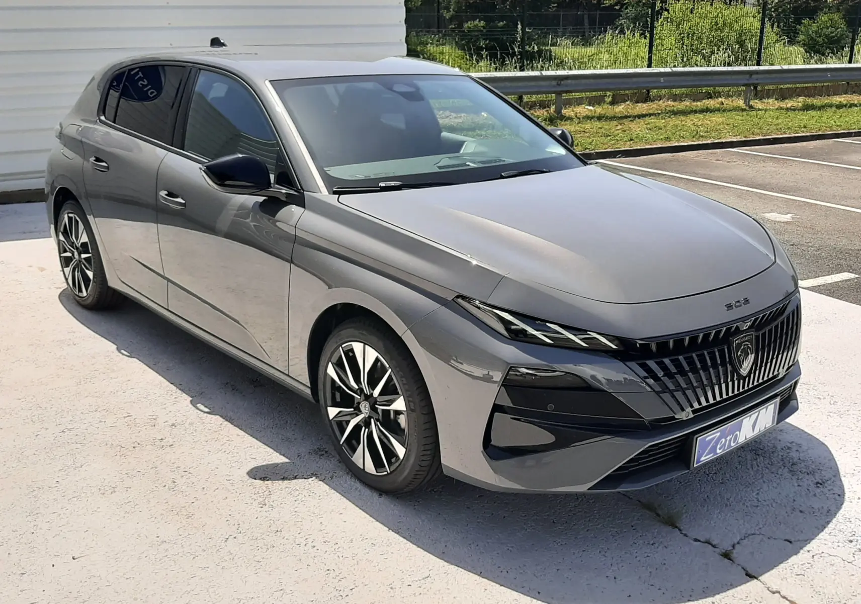 Peugeot 308 gris sélénium vue 3/4 avant droit, avec calandre noire distinctive et jantes bicolores.