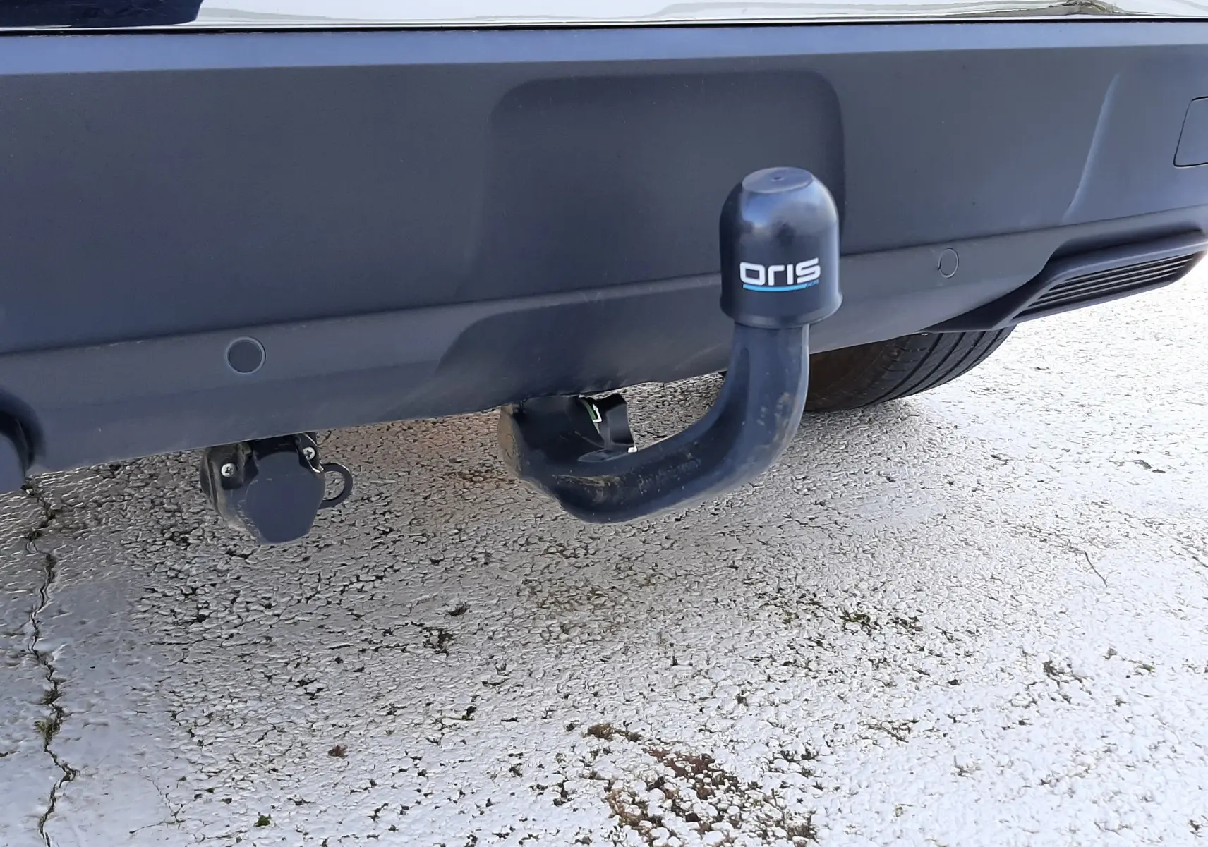 Gros plan sur l'attelage de remorque noir fixé au pare-chocs arrière gris platinium d'un Peugeot 3008 2023.