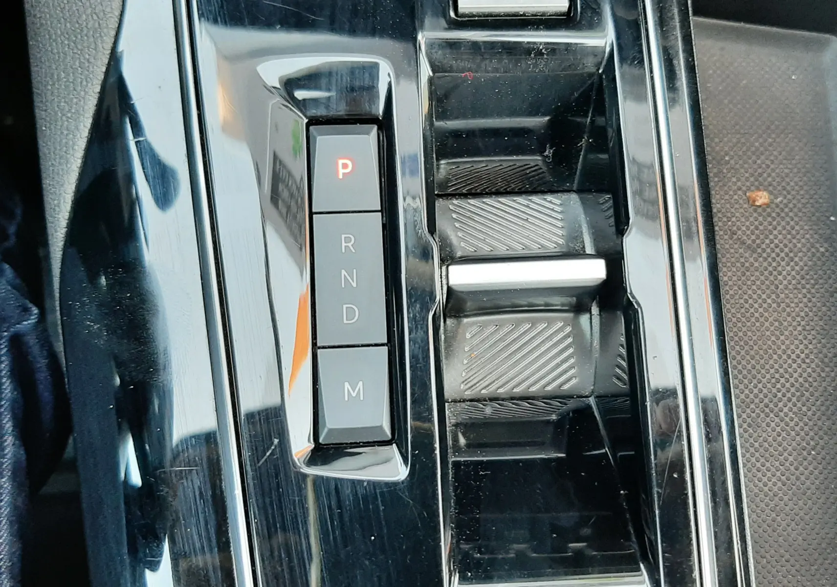 Gros plan sur la console centrale noire brillante du Peugeot 3008 2023 avec sélecteur de boîte auto et bouton Drive Mode.